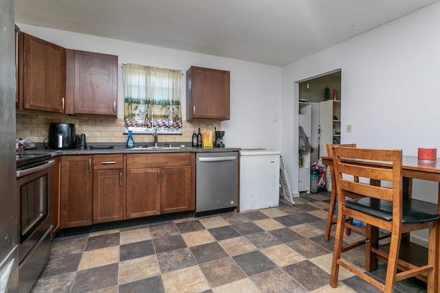 kitchen with decorative backsplash, dark countertops, appliances with stainless steel finishes, stone finish flooring, and a sink