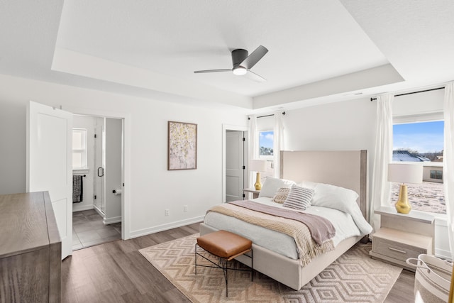 bedroom with hardwood / wood-style flooring, ceiling fan, connected bathroom, and a raised ceiling