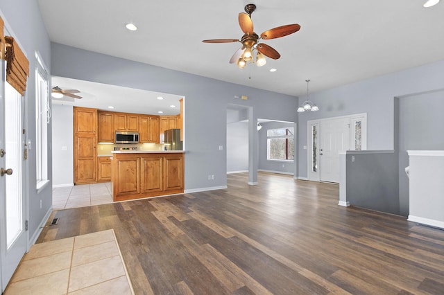 unfurnished living room with ceiling fan with notable chandelier and light hardwood / wood-style floors