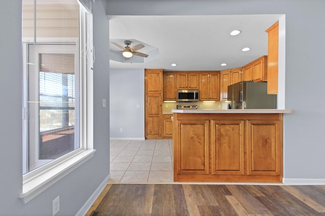 kitchen with black refrigerator, ceiling fan, light wood-type flooring, kitchen peninsula, and range