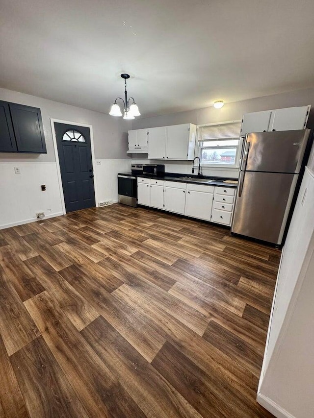 kitchen with white cabinets, appliances with stainless steel finishes, dark wood-type flooring, decorative light fixtures, and a sink