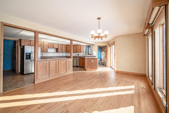 kitchen featuring decorative light fixtures, decorative backsplash, light hardwood / wood-style flooring, stainless steel appliances, and a chandelier