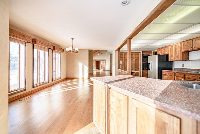 kitchen with stainless steel refrigerator with ice dispenser, sink, hanging light fixtures, light wood-type flooring, and a chandelier