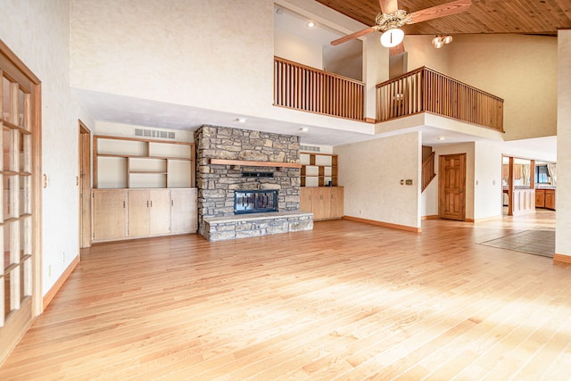 unfurnished living room featuring a high ceiling, built in shelves, a fireplace, light wood-type flooring, and ceiling fan