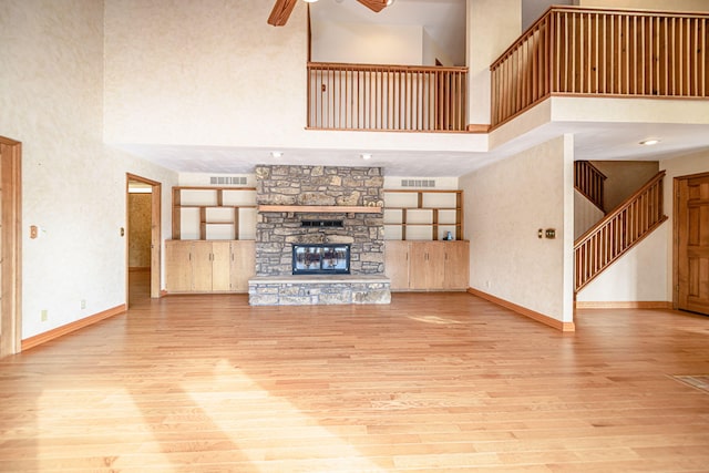 unfurnished living room with ceiling fan, a high ceiling, a stone fireplace, and light wood-type flooring