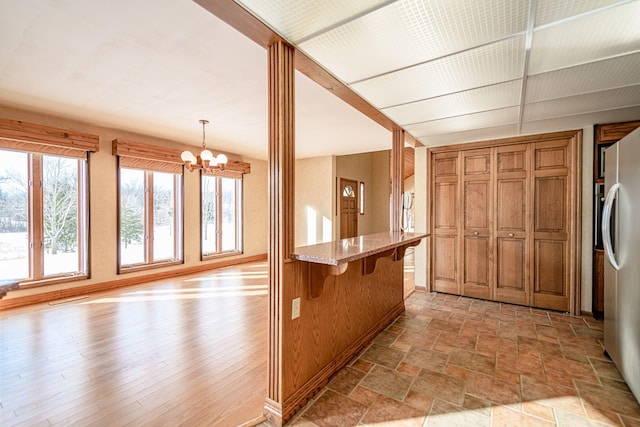 kitchen with light stone countertops, pendant lighting, a kitchen breakfast bar, a chandelier, and stainless steel refrigerator