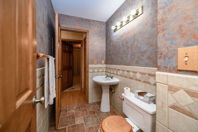 bathroom with toilet, tile walls, sink, and a textured ceiling