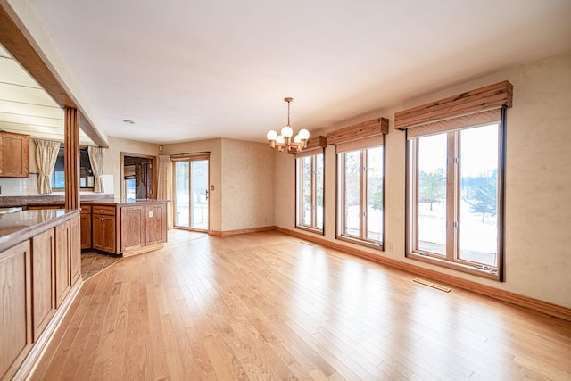 interior space with light wood-type flooring, an inviting chandelier, plenty of natural light, and decorative light fixtures