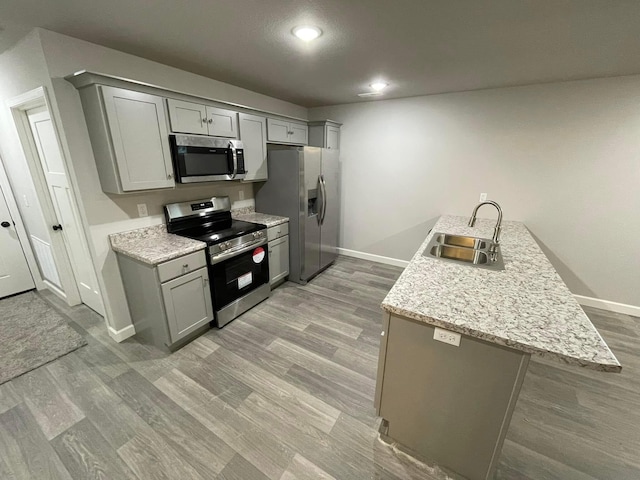 kitchen with light stone counters, gray cabinetry, stainless steel appliances, sink, and light hardwood / wood-style floors