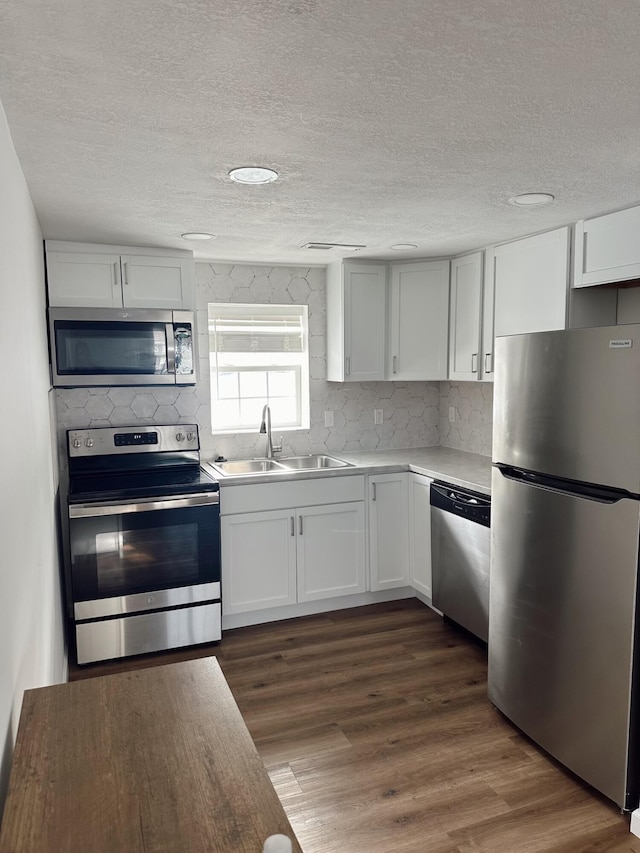 kitchen featuring sink, dark wood-type flooring, appliances with stainless steel finishes, white cabinetry, and a textured ceiling