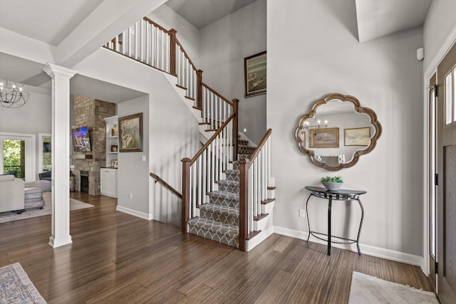 entryway featuring an inviting chandelier, a stone fireplace, dark hardwood / wood-style floors, ornate columns, and a towering ceiling