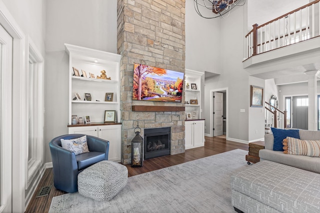 living room featuring built in features, a high ceiling, a stone fireplace, and dark wood-type flooring