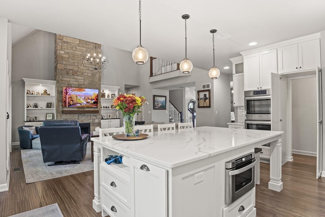 kitchen featuring light stone countertops, a kitchen island, pendant lighting, a fireplace, and white cabinetry