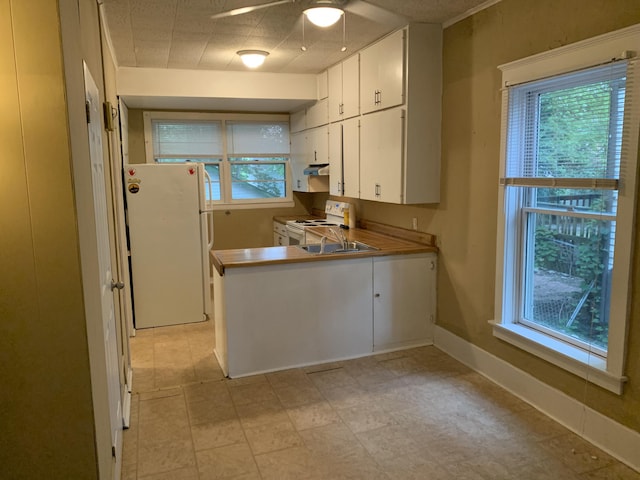 kitchen with under cabinet range hood, white cabinetry, white appliances, a peninsula, and baseboards