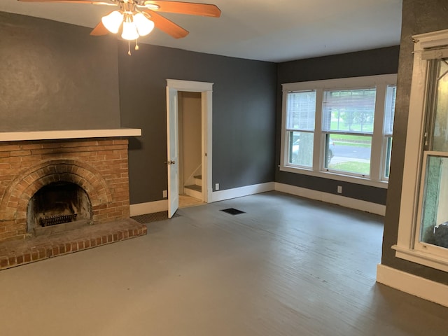 unfurnished living room with a brick fireplace, baseboards, visible vents, and ceiling fan