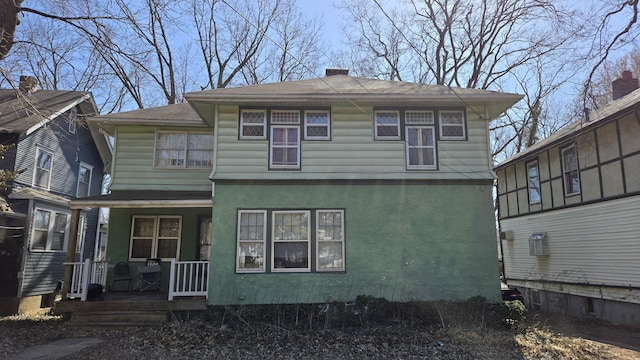 rear view of property with stucco siding, covered porch, and a chimney