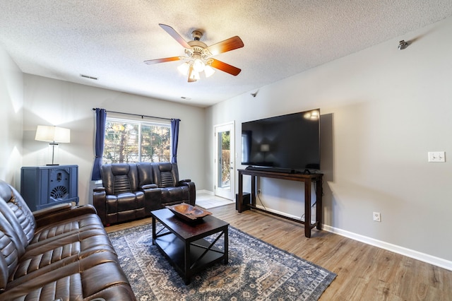 living room with a textured ceiling, ceiling fan, and wood-type flooring