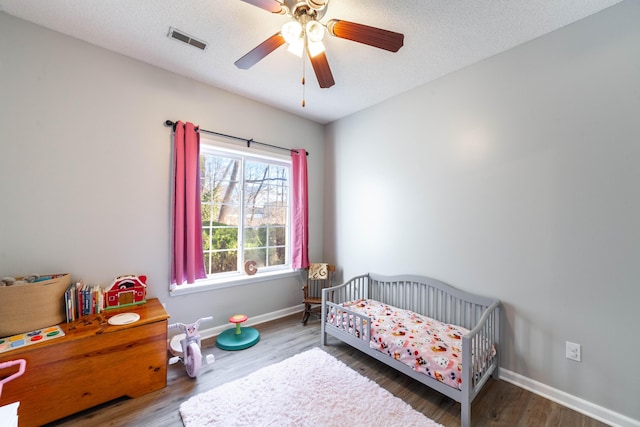 bedroom featuring ceiling fan, a nursery area, dark hardwood / wood-style floors, and a textured ceiling