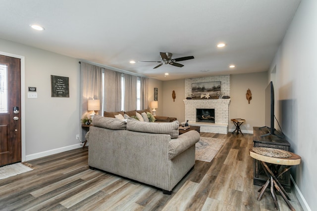 living room with a healthy amount of sunlight, ceiling fan, dark hardwood / wood-style flooring, and a brick fireplace