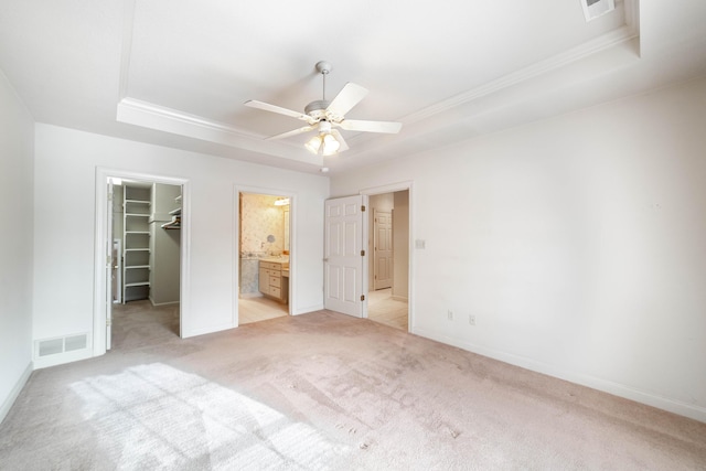 unfurnished bedroom featuring a raised ceiling, light colored carpet, ceiling fan, and ensuite bathroom