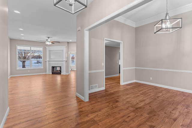 unfurnished living room with ceiling fan with notable chandelier, wood-type flooring, and crown molding