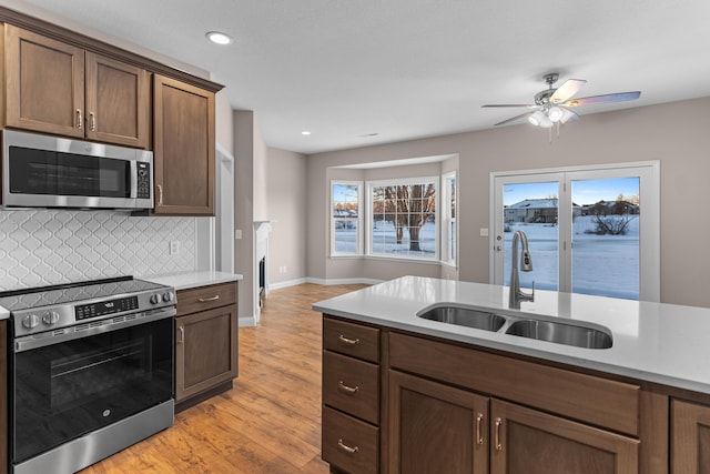 kitchen with light hardwood / wood-style floors, tasteful backsplash, appliances with stainless steel finishes, dark brown cabinets, and sink