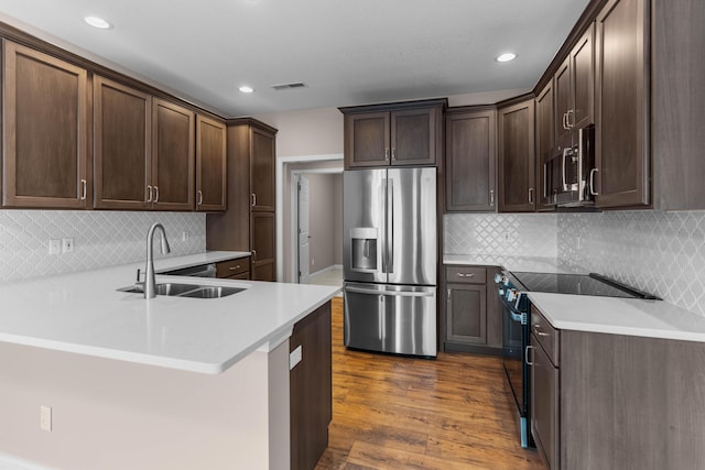 kitchen with kitchen peninsula, dark wood-type flooring, stainless steel appliances, decorative backsplash, and sink