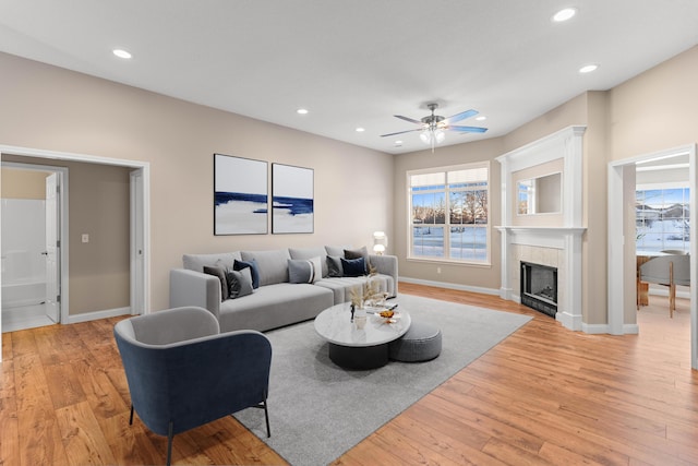 living room featuring plenty of natural light, light hardwood / wood-style floors, a tile fireplace, and ceiling fan