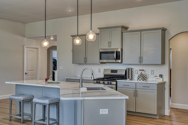 kitchen featuring appliances with stainless steel finishes, pendant lighting, a kitchen island with sink, and gray cabinets