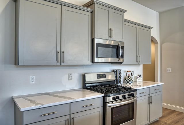 kitchen featuring light stone counters, appliances with stainless steel finishes, gray cabinets, and dark hardwood / wood-style floors