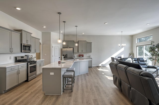 kitchen with decorative light fixtures, appliances with stainless steel finishes, gray cabinets, and a breakfast bar