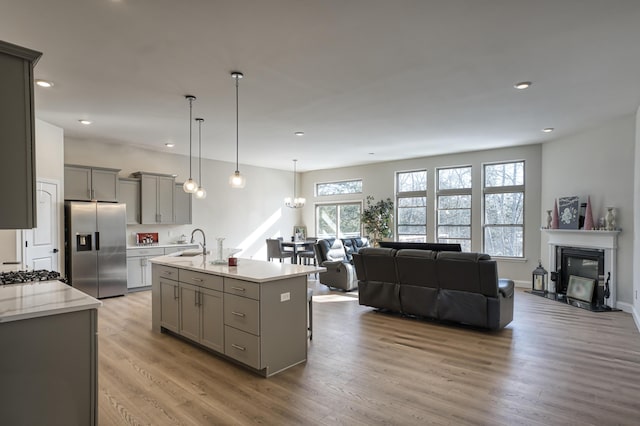 kitchen featuring a kitchen island with sink, gray cabinetry, stainless steel appliances, light wood-type flooring, and sink