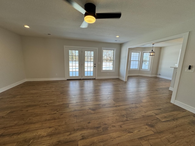 empty room with a textured ceiling, dark wood-type flooring, and ceiling fan with notable chandelier