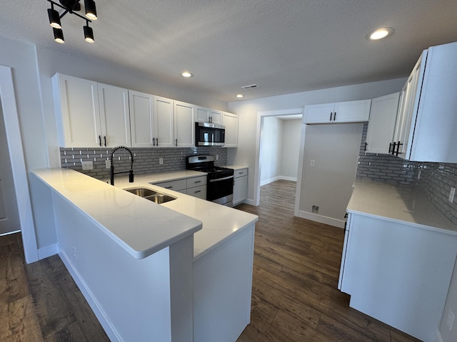 kitchen with appliances with stainless steel finishes, white cabinetry, sink, backsplash, and kitchen peninsula