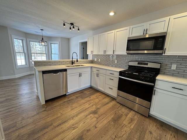 kitchen featuring white cabinetry, kitchen peninsula, appliances with stainless steel finishes, decorative light fixtures, and sink