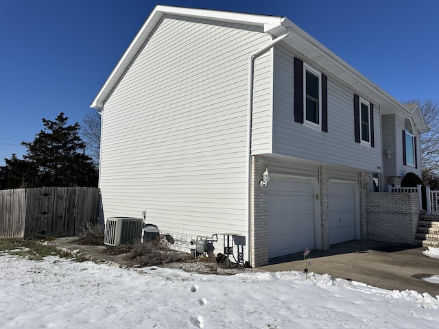 snow covered property featuring a garage and central AC