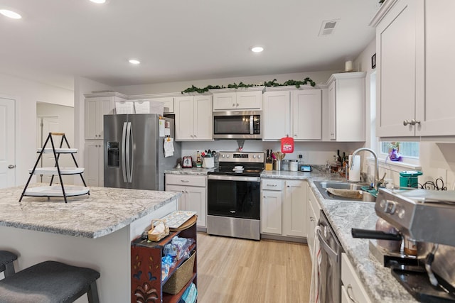 kitchen with sink, a breakfast bar area, light hardwood / wood-style flooring, appliances with stainless steel finishes, and white cabinets