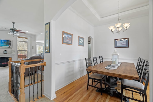 dining room with a tray ceiling, ceiling fan with notable chandelier, ornamental molding, and light hardwood / wood-style floors