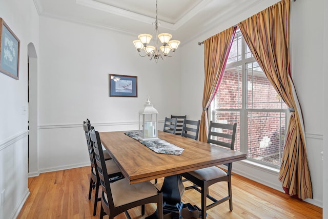 dining space with arched walkways, a chandelier, light wood-style flooring, a raised ceiling, and crown molding