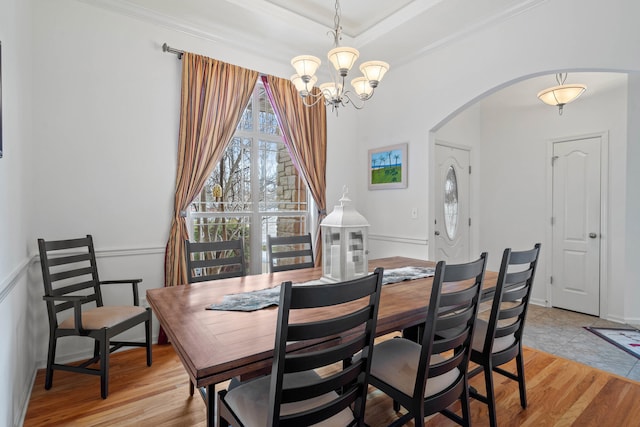 dining room featuring ornamental molding, arched walkways, a notable chandelier, and light wood finished floors