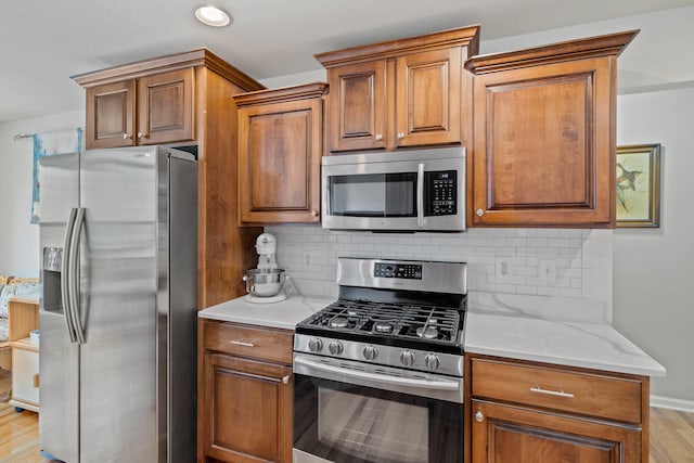 kitchen with light wood-type flooring, backsplash, appliances with stainless steel finishes, and light stone countertops