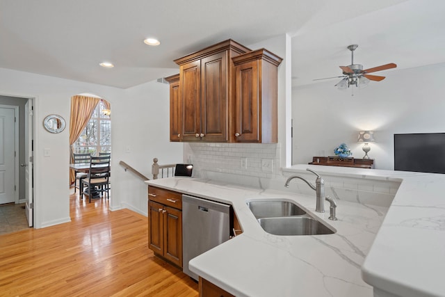 kitchen with arched walkways, a sink, light wood-style floors, stainless steel dishwasher, and decorative backsplash