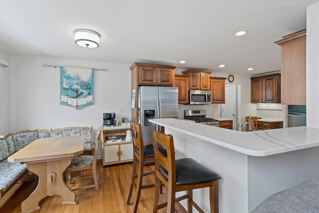 kitchen with tasteful backsplash, kitchen peninsula, light wood-type flooring, a breakfast bar area, and stainless steel appliances