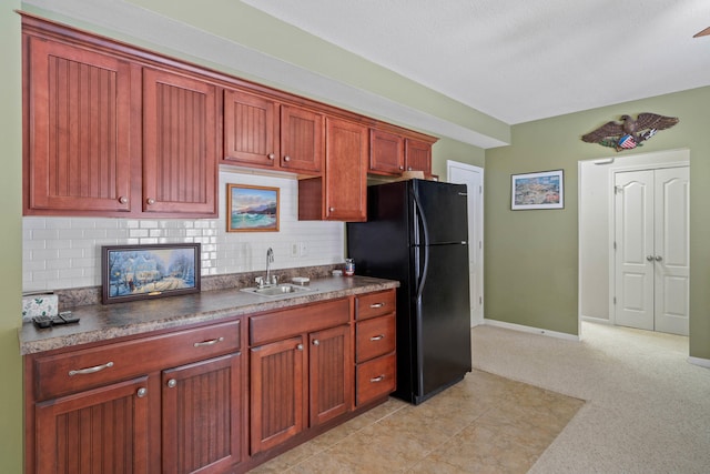 kitchen featuring a sink, baseboards, freestanding refrigerator, decorative backsplash, and dark countertops