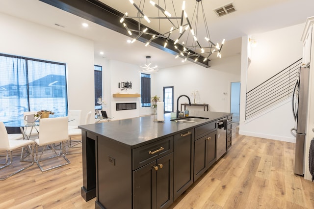 kitchen with pendant lighting, appliances with stainless steel finishes, sink, a kitchen island with sink, and light wood-type flooring