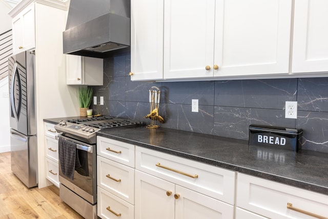 kitchen with appliances with stainless steel finishes, wall chimney exhaust hood, white cabinets, and backsplash