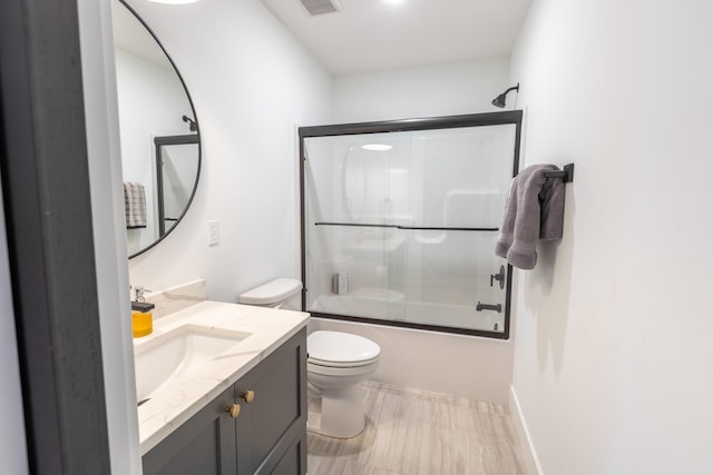 full bathroom featuring toilet, bath / shower combo with glass door, and vanity