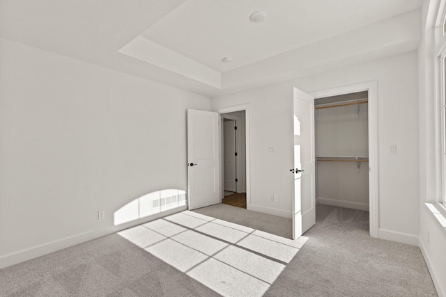 unfurnished bedroom featuring a raised ceiling, light colored carpet, and a closet