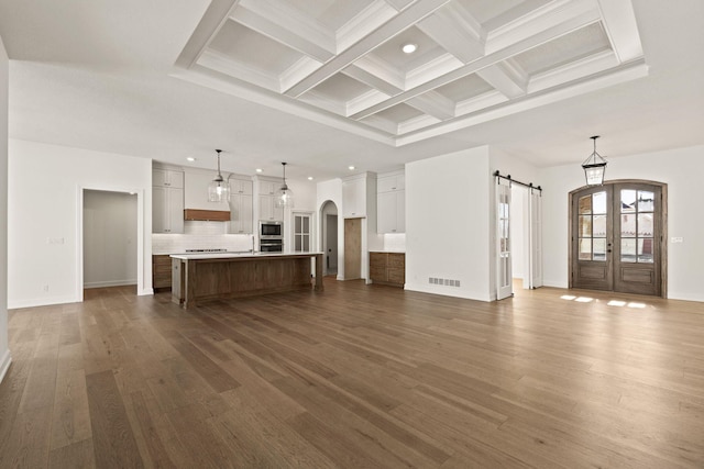 unfurnished living room with dark hardwood / wood-style flooring, a barn door, coffered ceiling, and beamed ceiling