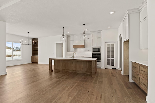 kitchen featuring white cabinetry, sink, a large island, oven, and built in microwave